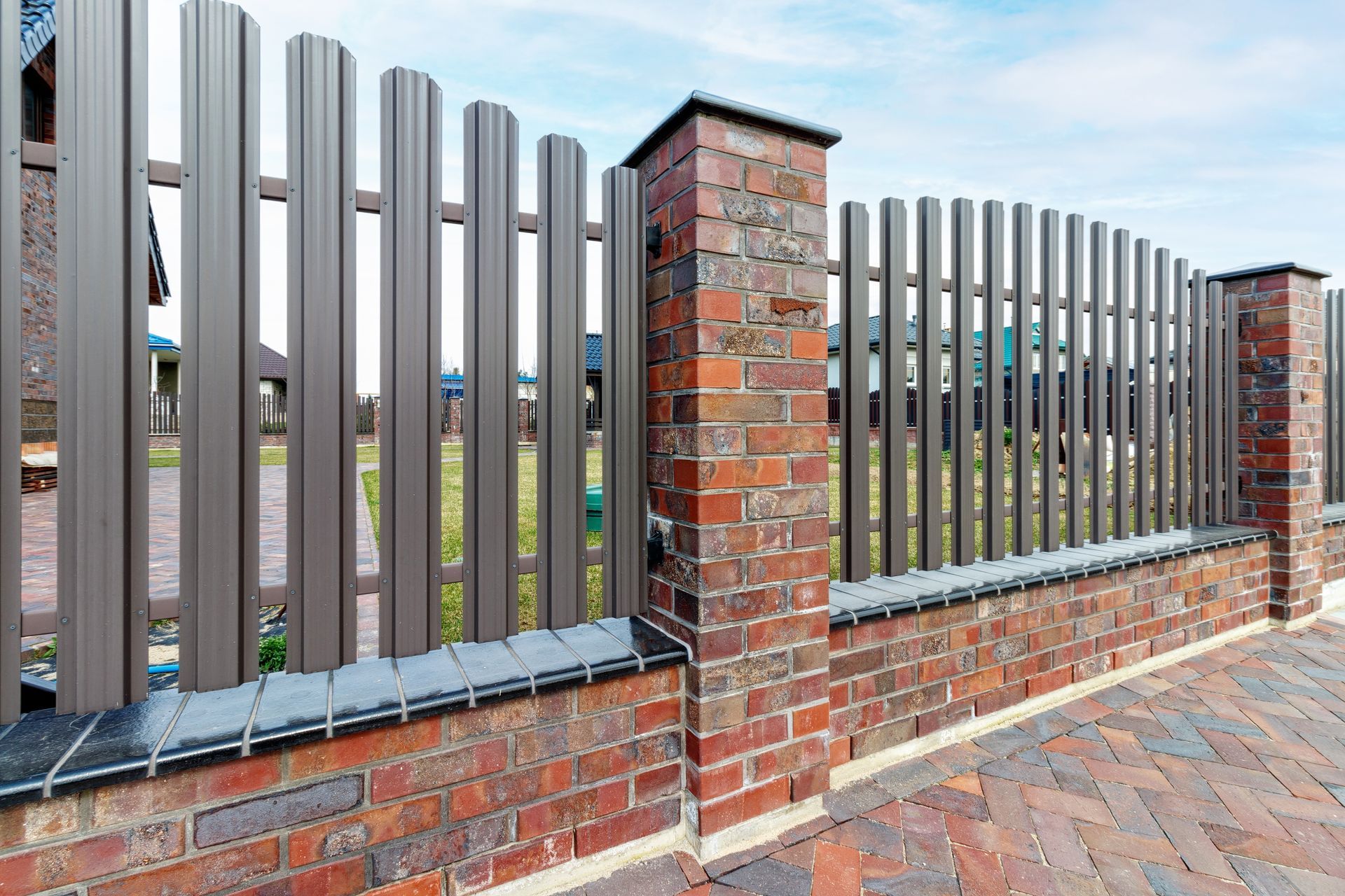 Brown brick and metal fence with arched top and brick pillars against a blue sky.