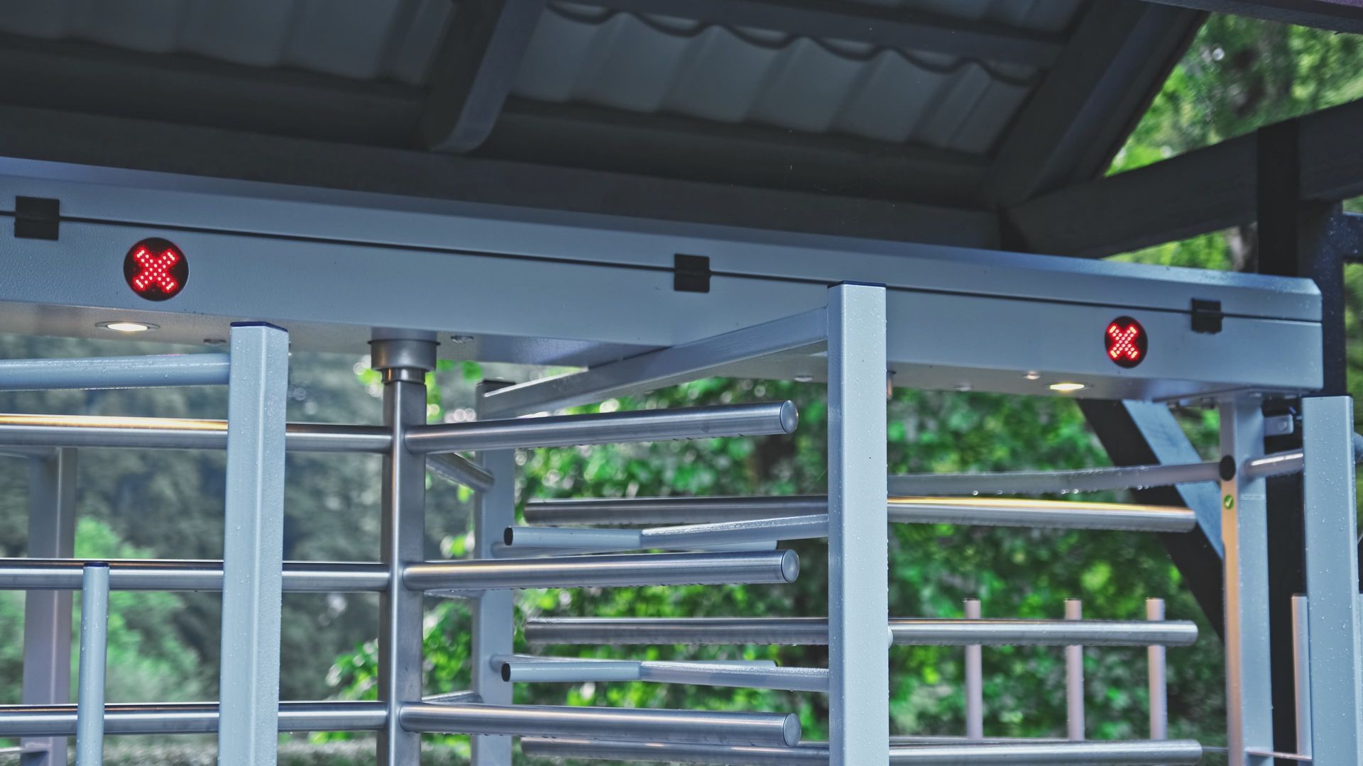 Turnstile with red X lights, under a covered structure, with trees in the background.