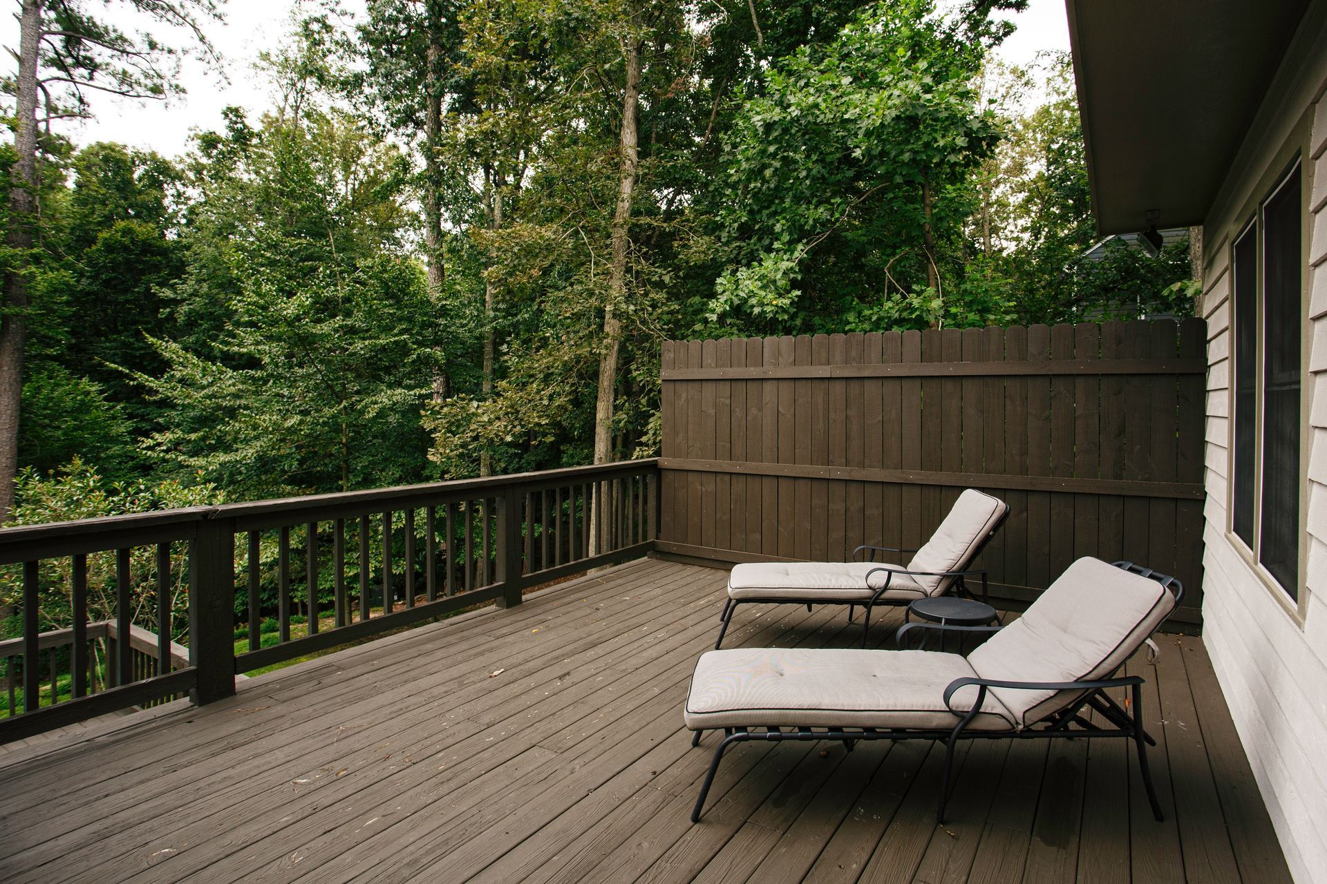 Wooden deck with two lounge chairs, overlooking a forest.