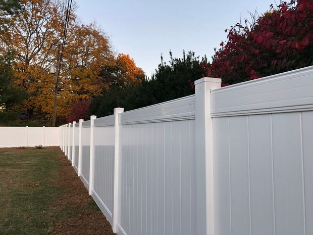 White vinyl fence along a grassy lawn with trees and colorful fall foliage in the background.