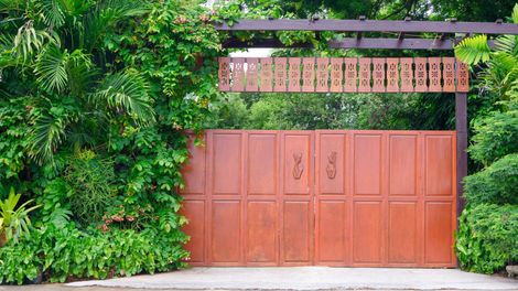 Brown gate with carved header, surrounded by lush green foliage.