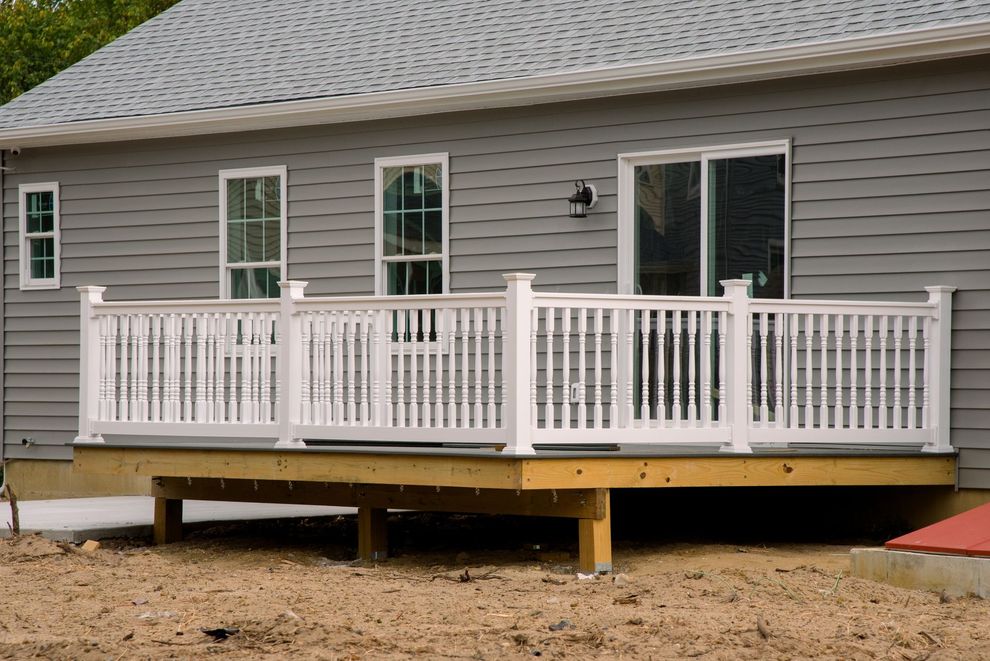 White railing on a wooden deck attached to a gray house with windows and a sliding door.