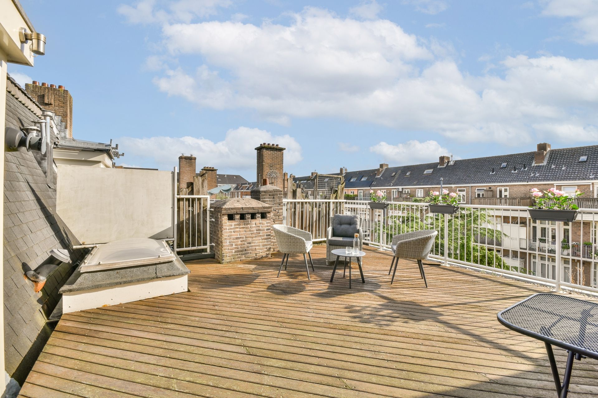 Rooftop deck with seating, overlooking city buildings, blue sky with clouds.