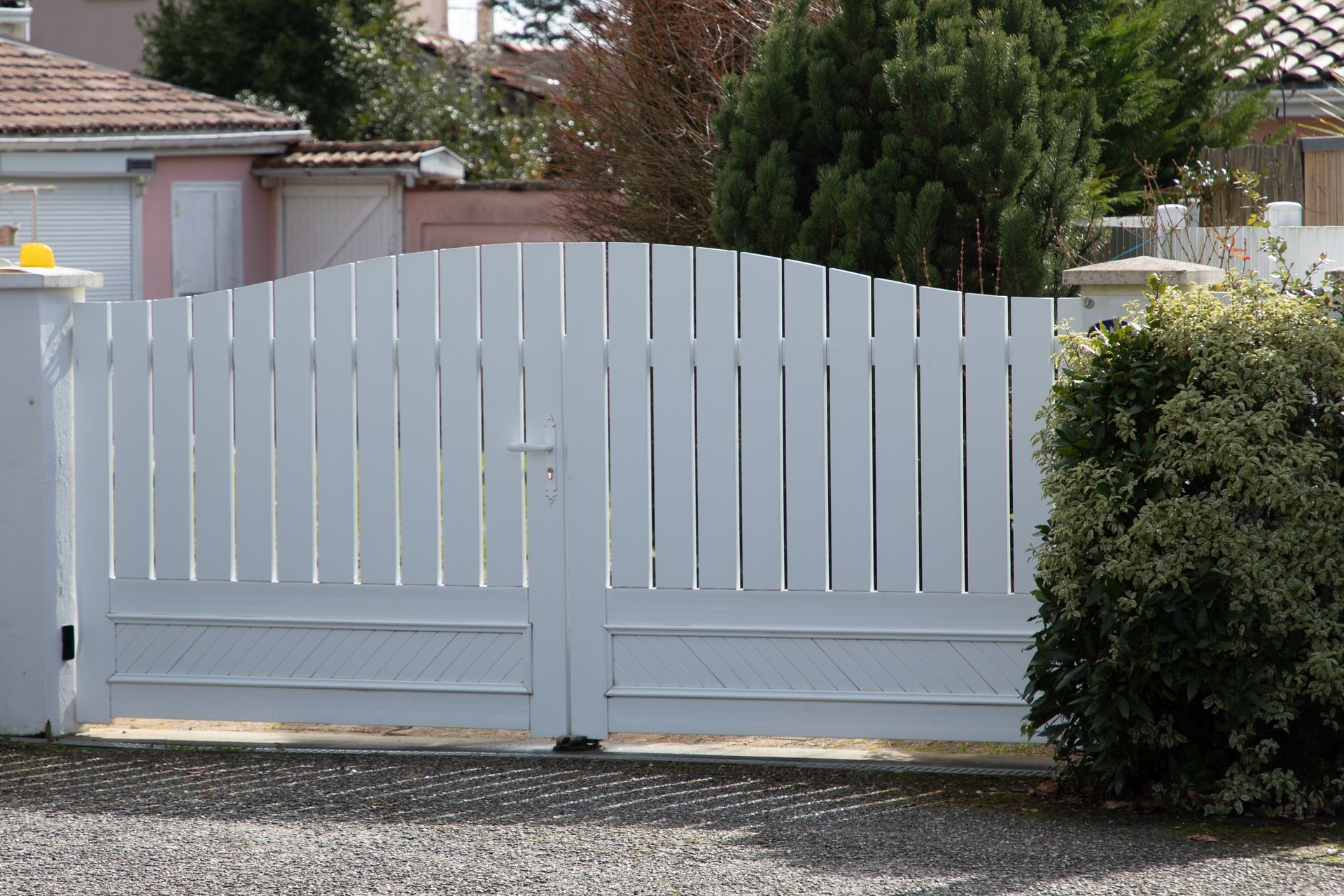 White wooden gate with arched top, leading to a property, gravel driveway.