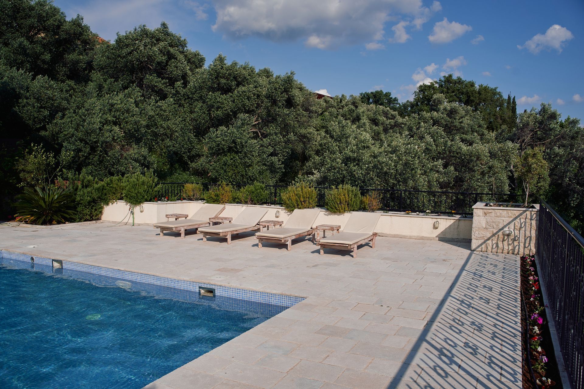 Poolside with lounge chairs, overlooking a lush green hillside on a sunny day.