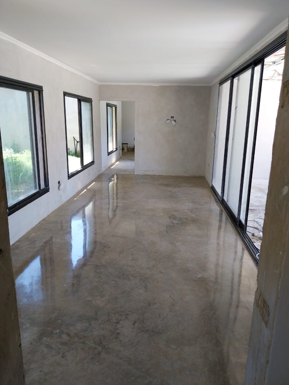 Habitación vacía con suelo de hormigón pulido y grandes ventanales que reflejan la luz.