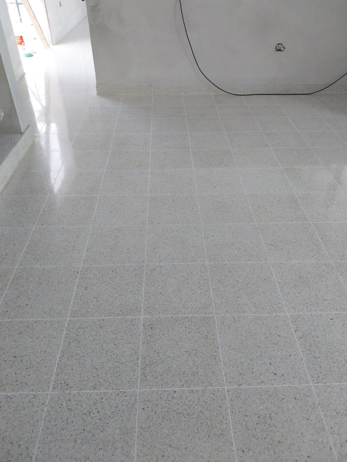 Suelo de baldosas de color gris claro en una habitación, con un atisbo de una puerta abierta y paredes blancas.