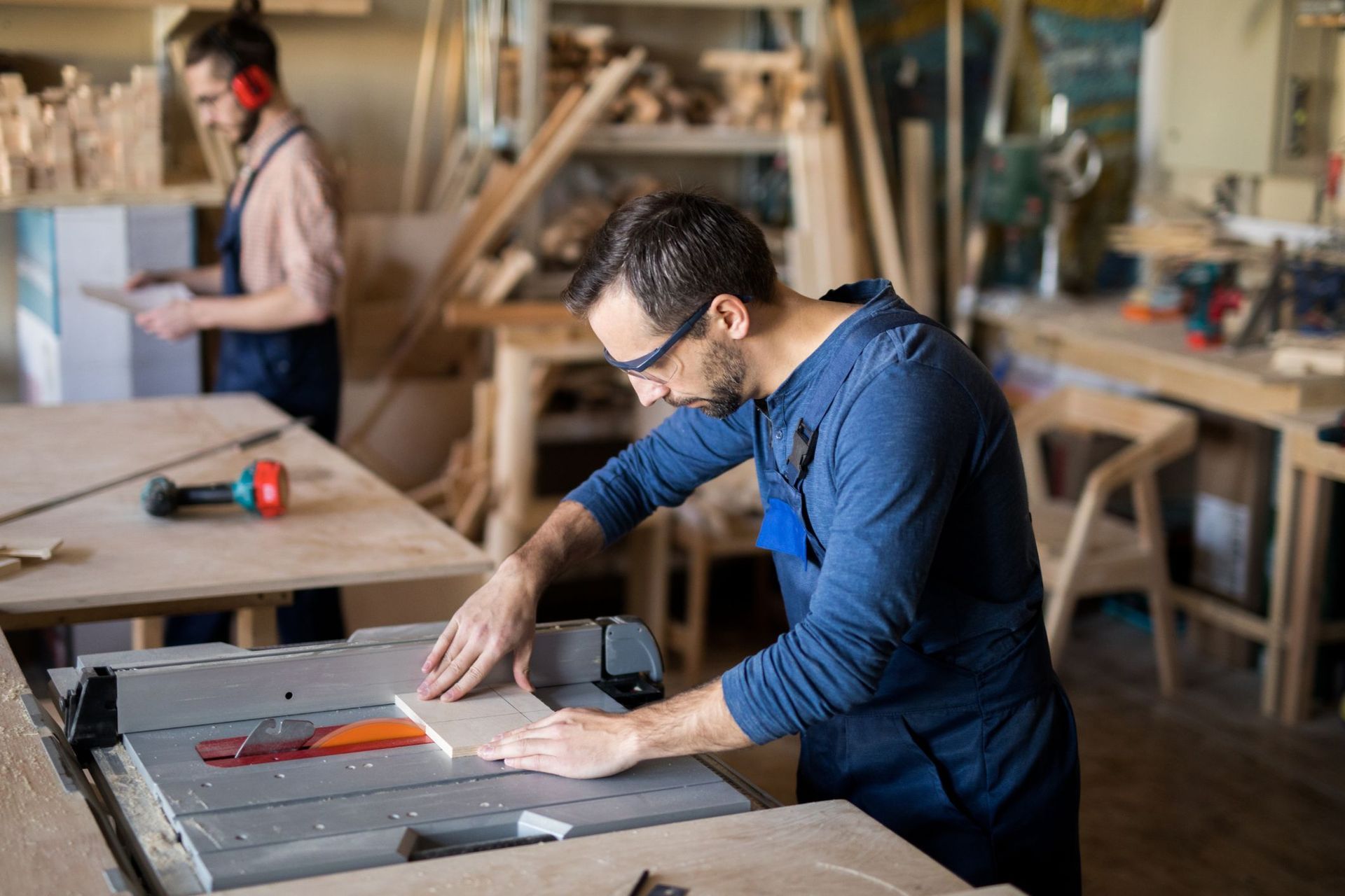 A man is cutting a piece of wood on a table saw in a workshop.