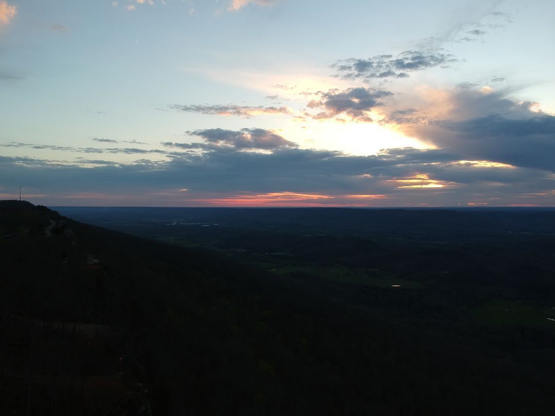 A sunset over a valley with a mountain in the foreground