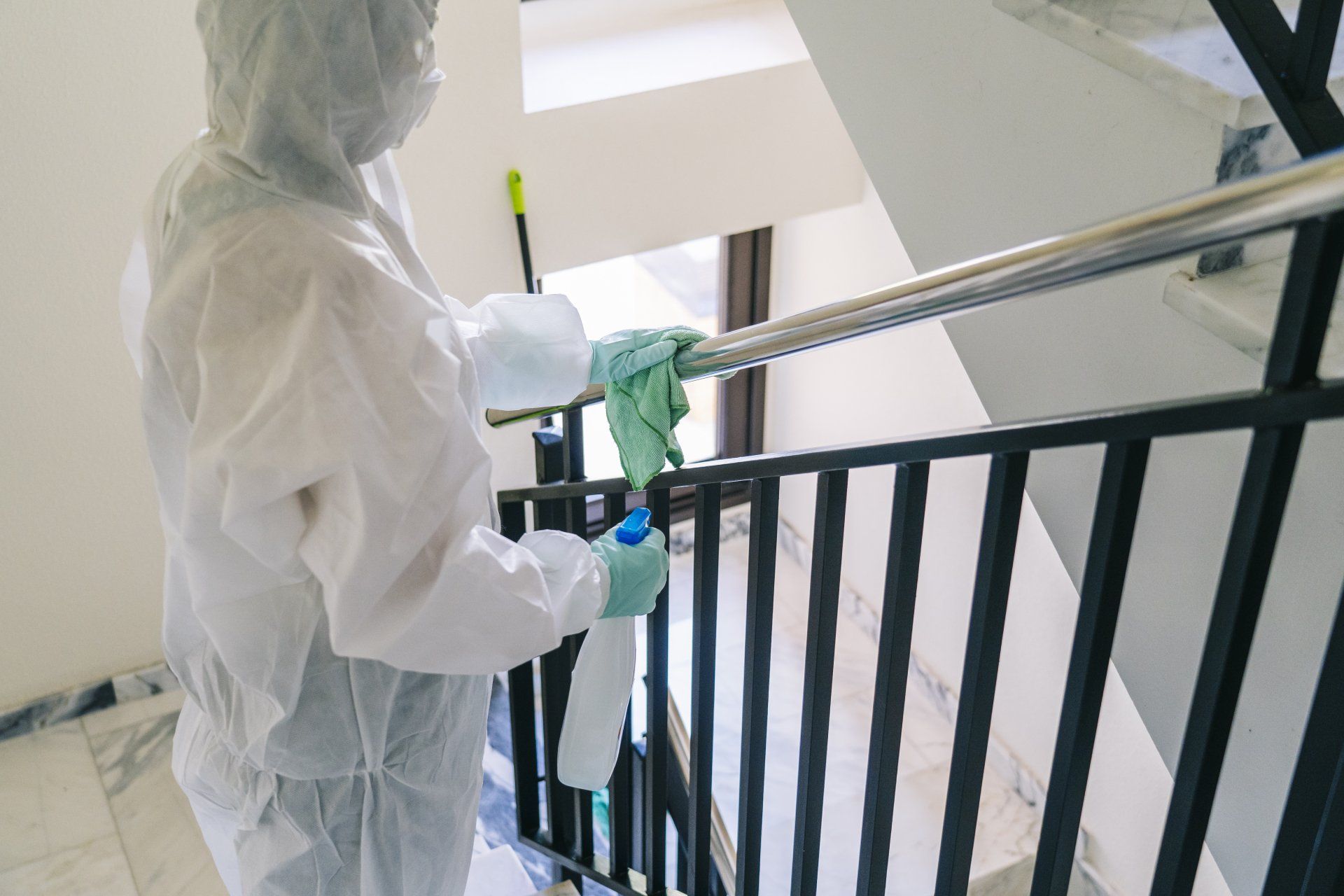 Worker in Safety Suit Sanitizing Stairway Railing