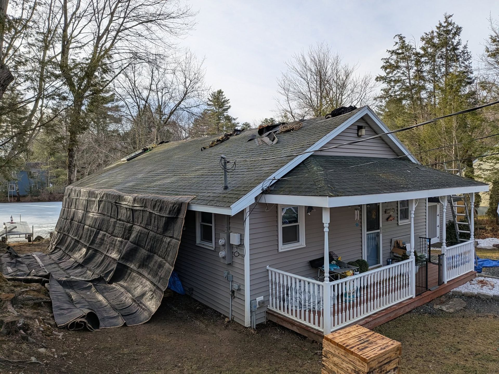 Gray shingled roof under blue sky with clouds and a leafy green tree nearby