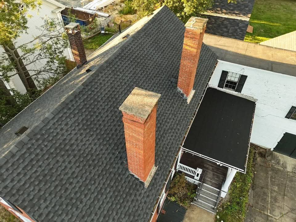 Brick chimney flashing on a gray shingled roof with stepped metal siding trim