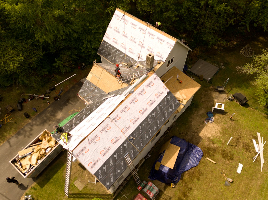 Workers reroofing a house, removing old shingles from a dark roof