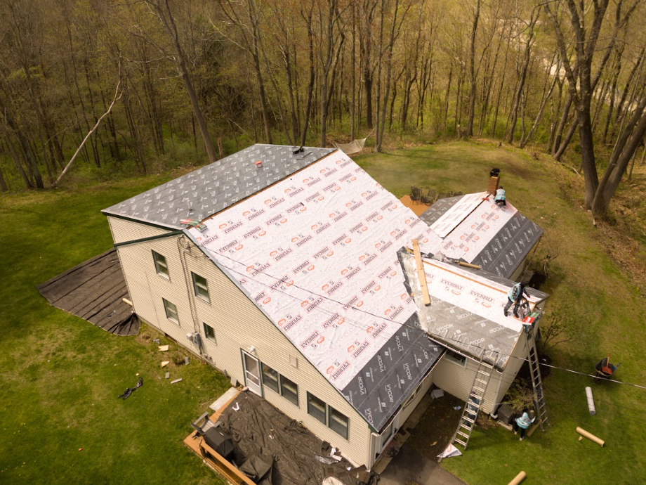 Aerial view of a house under construction with roof underlayment in a wooded area