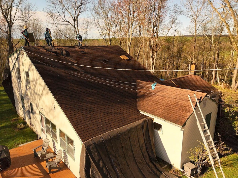 Severely tilted house roof with workers on top and a ladder leaning against the side