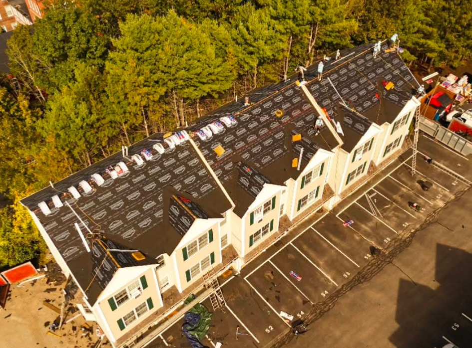 Aerial view of a row of townhouses with black roofs and parking spaces beside trees