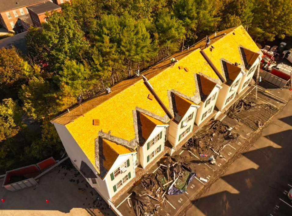 Aerial view of a building with a bright yellow roof under construction, surrounded by trees and debris.