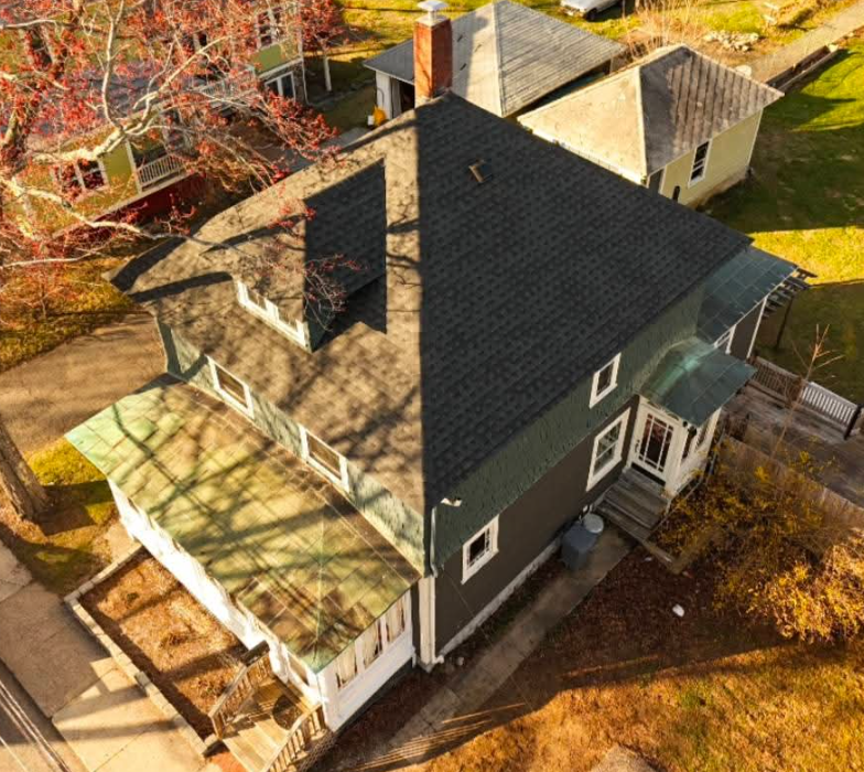 Aerial view of a dark-roofed house with a sunroom and deck surrounded by autumn trees