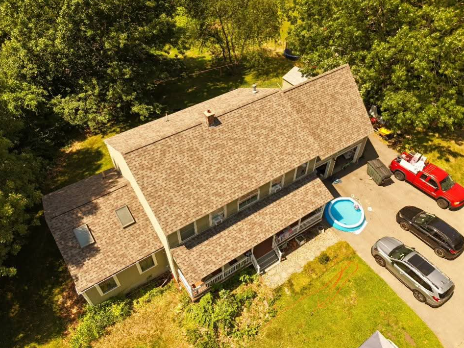 Aerial view of a tan-roofed house with a blue above-ground pool and parked cars in the driveway.