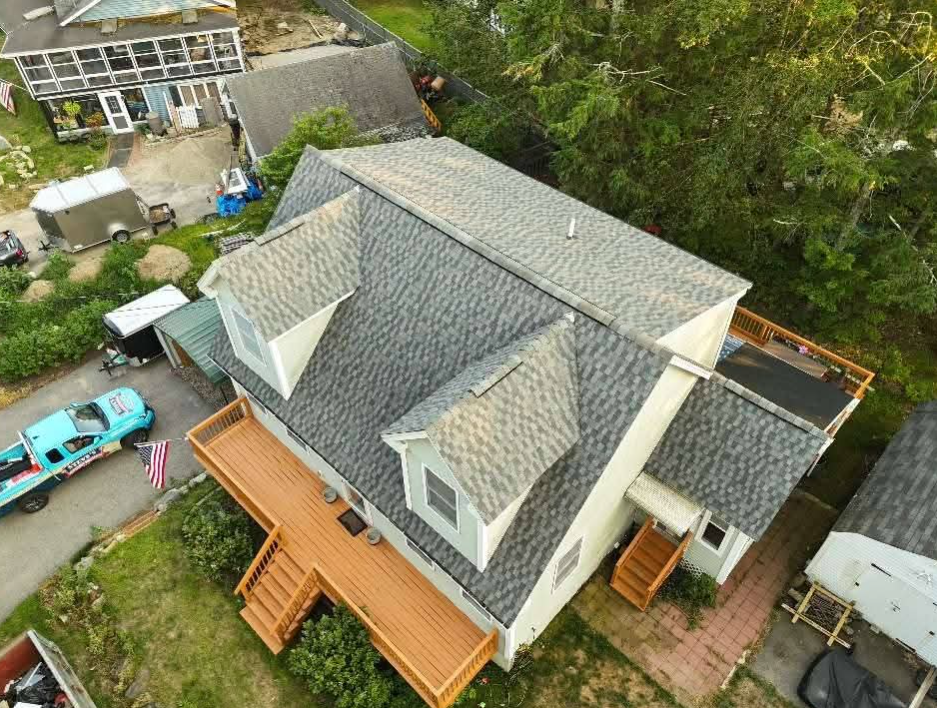 Aerial view of a gray-roofed house with a wooden deck, steps, and a turquoise car parked beside it.