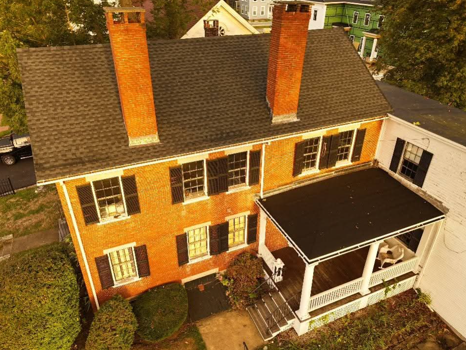 Aerial view of a yellow brick house with two chimneys and a white porch roof.