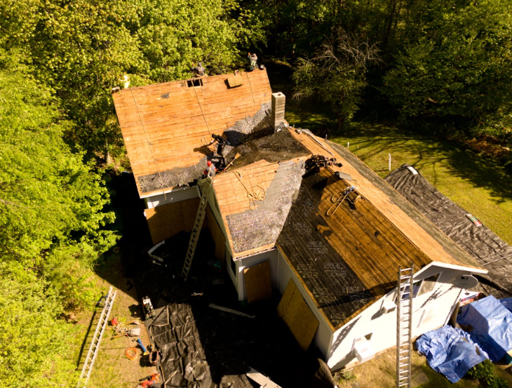 Aerial view of a damaged, partially collapsed roof surrounded by trees and debris.