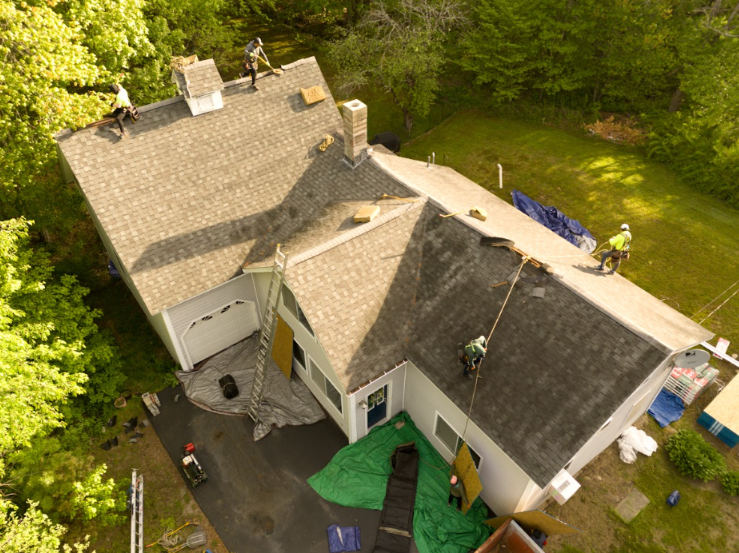 Aerial view of workers on a house roof, with blue tarps and a driveway below.