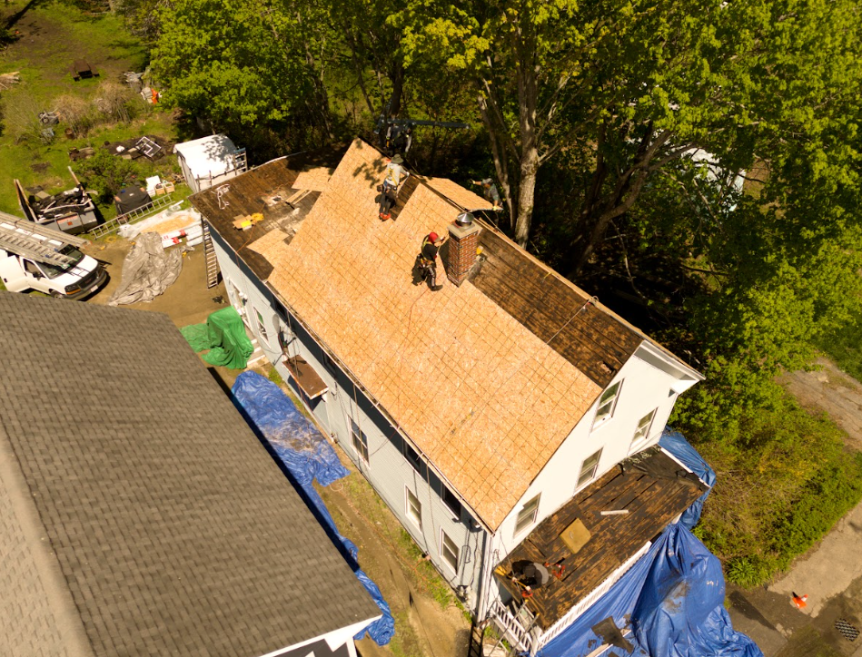 Roofing materials on black shingles: rolled underlayment and metal flashing beside exposed OSB decking