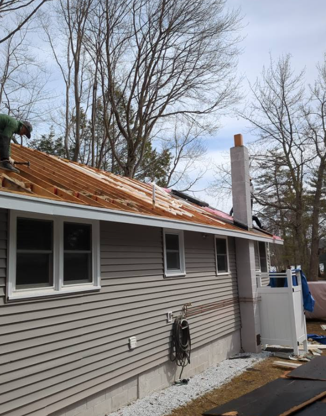 Roof being repaired on a beige house with exposed plywood and a chimney under a cloudy sky