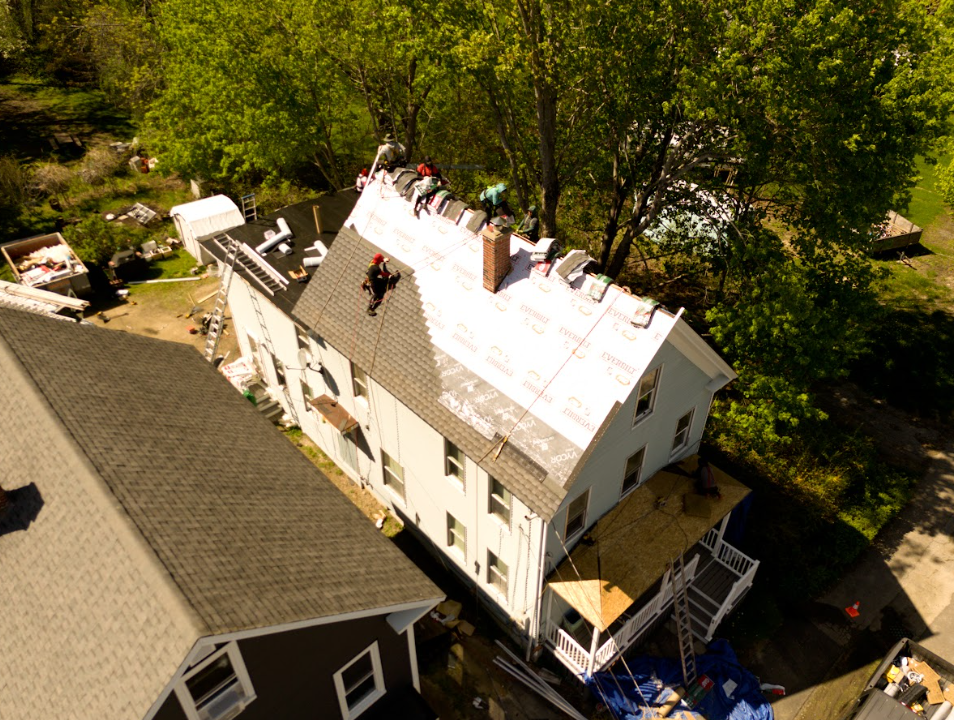 Aerial view of a house with a white roof being repaired, with workers on top and scaffolding below
