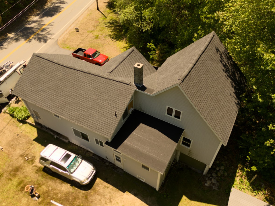 Aerial view of a gray house with two cars parked beside it and a red truck on the street.