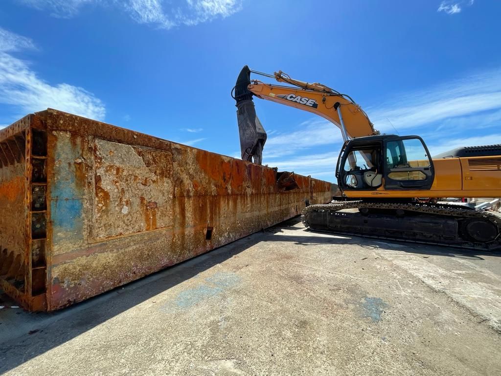 Un escavatore demolisce un'imbarcazione navale con struttura metallica arrugginita Riolo metalli Siracusa Sicilia 