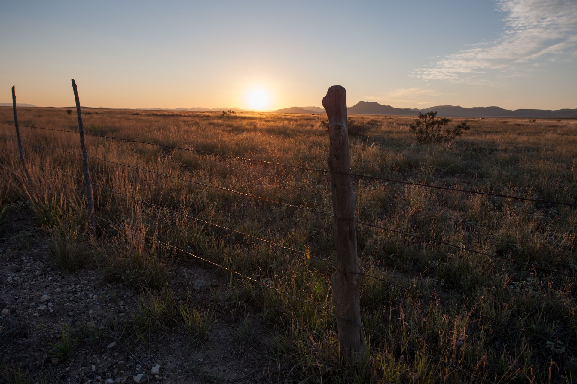 A wooden walkway leading to a gazebo overlooking a body of water at sunset.
