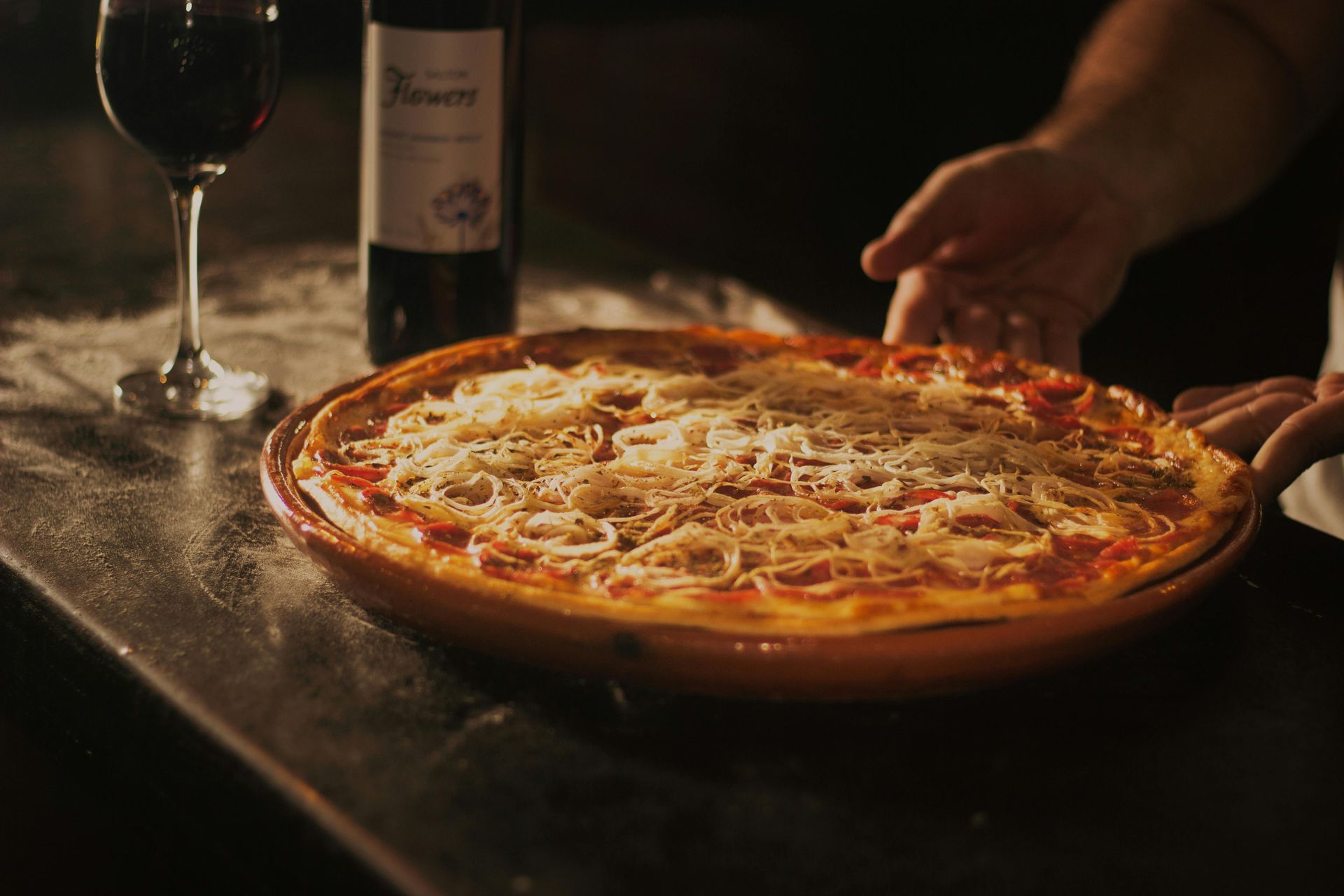 A pizza is sitting on a table next to a glass of wine and a bottle of wine.