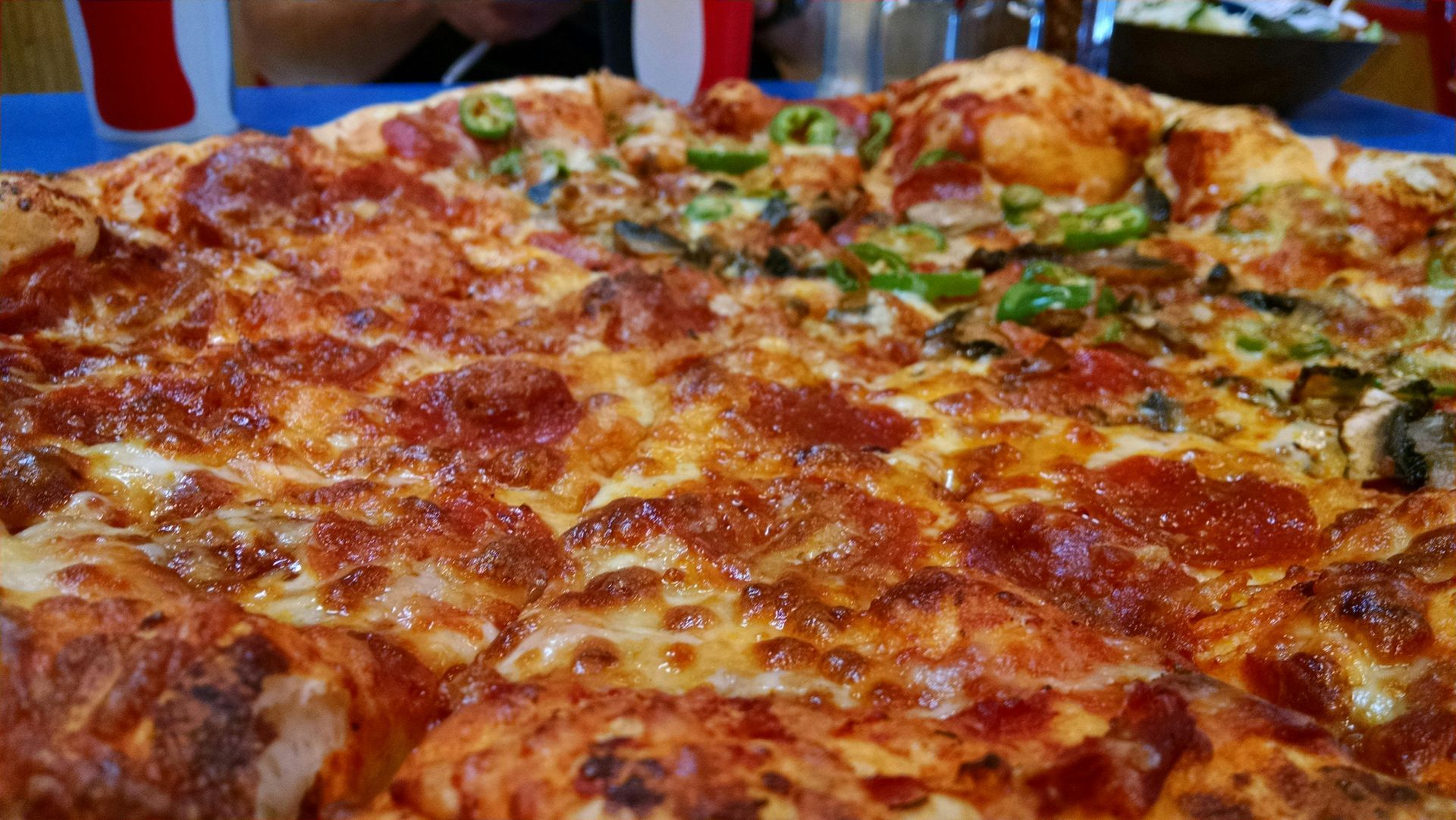 Close-up of a large pizza, half with pepperoni, half with green peppers and mushrooms.