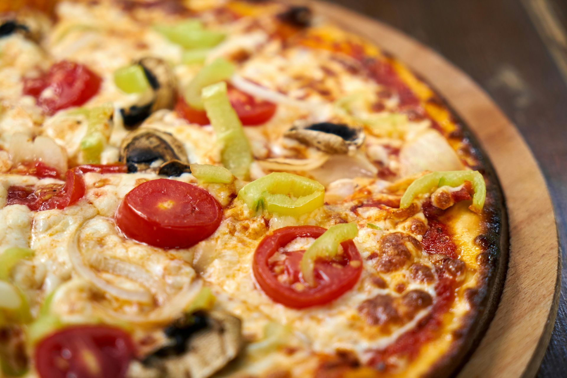 A pizza with tomatoes , peppers , mushrooms and cheese on a wooden cutting board.