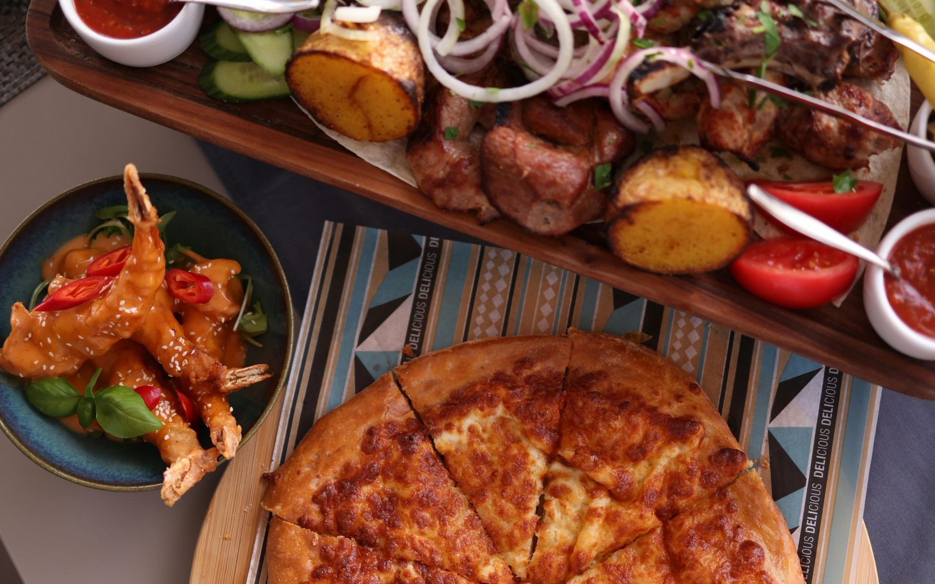 Assortment of grilled meat, potatoes, vegetables, and a cheese-filled bread. Shrimp with sauce and a bowl of dipping sauce.