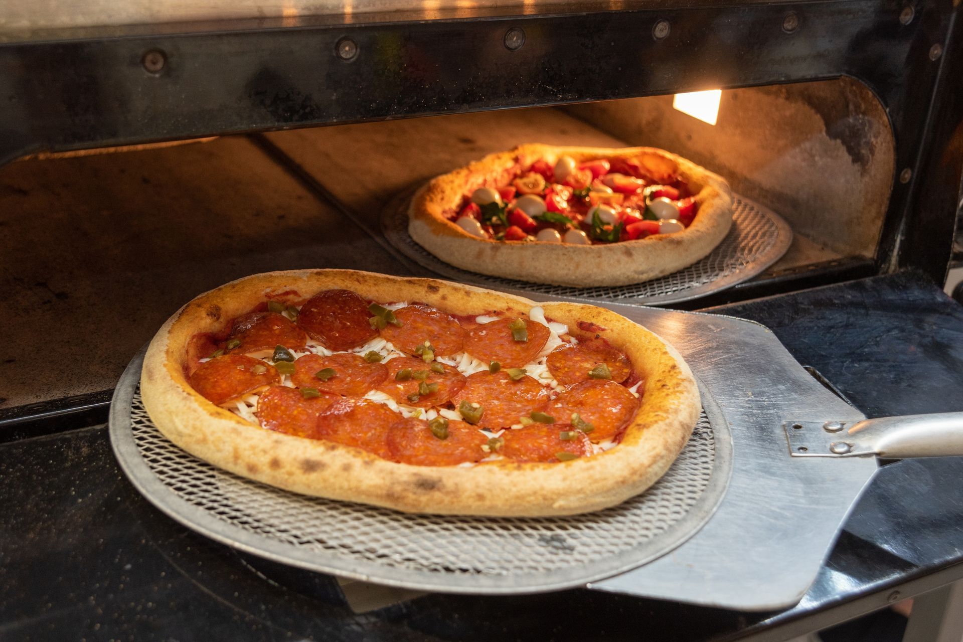 Two pizzas are being cooked in a pizza oven.