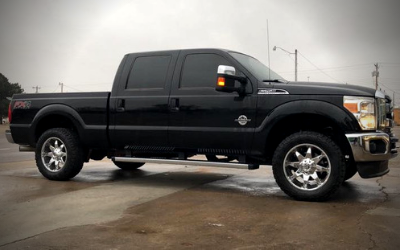 A black Ford Super Duty crew cab pickup truck parked on a paved lot under an overcast sky.