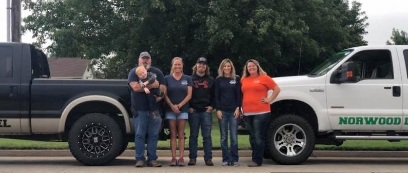 Five people stand between a dark truck and a white truck with