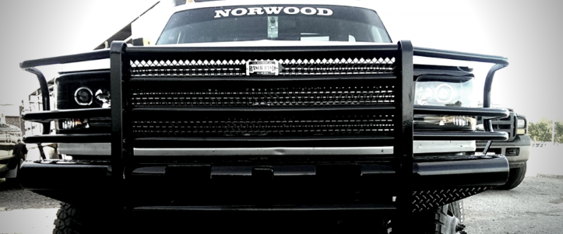 A black truck grille guard installed on the front of a white pickup truck, centered on the vehicle's front end.