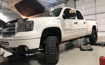 A white GMC truck with its hood open in a garage, undergoing maintenance with tools and spare parts nearby.