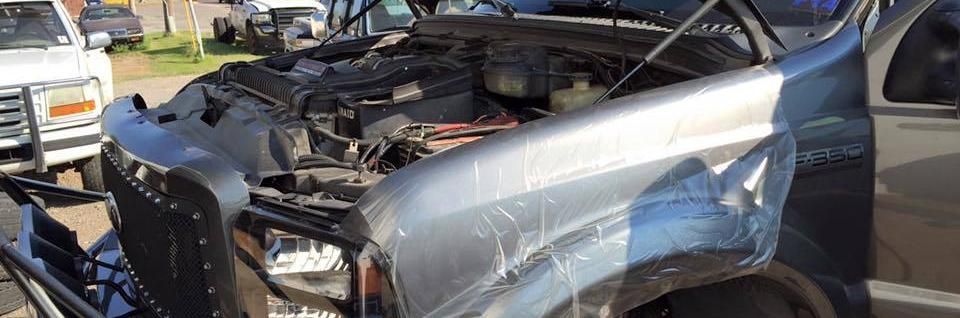 A gray pickup truck with an open hood, damaged front bodywork, and a black aftermarket grille guard.
