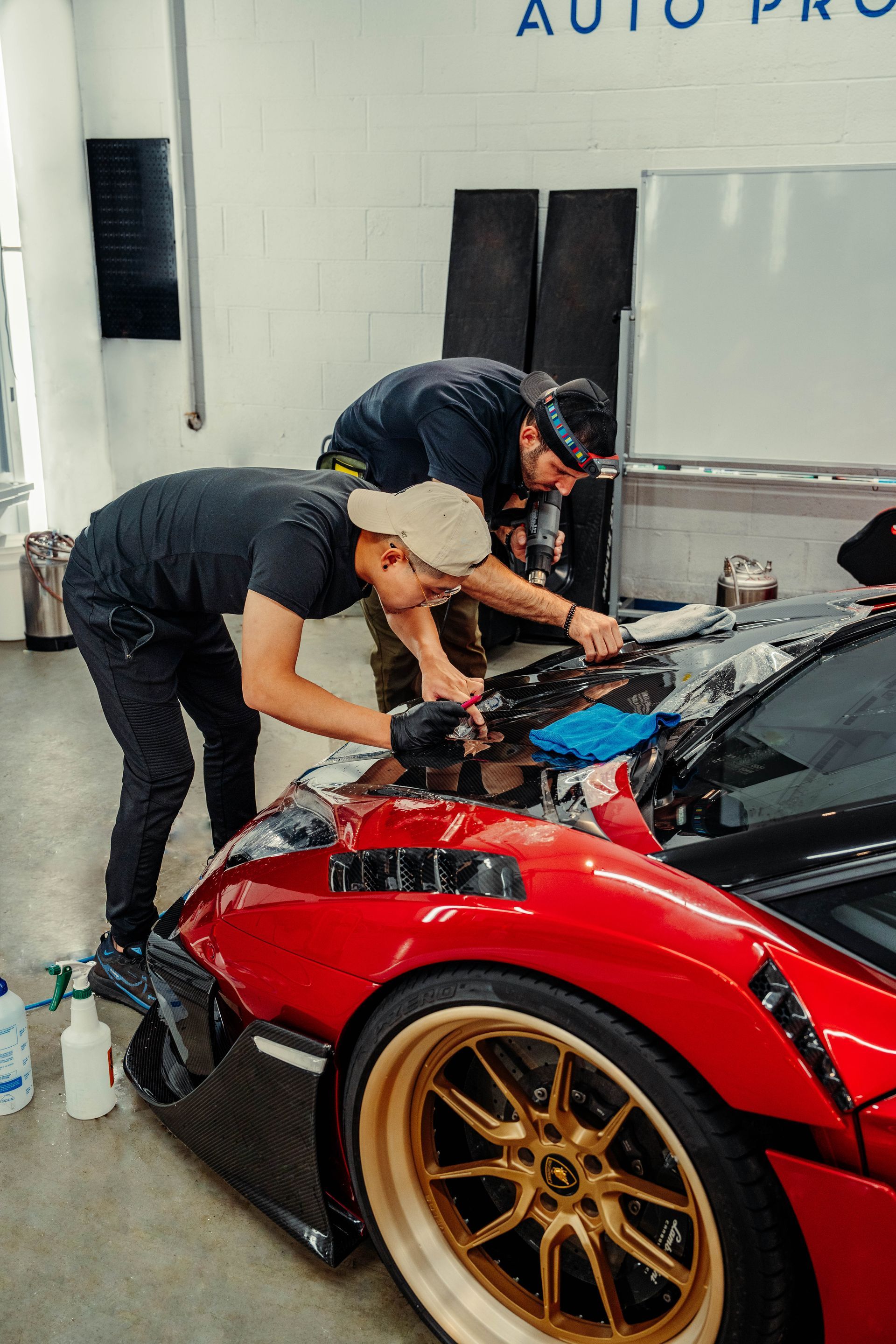 Two men are working on a red sports car in a garage.