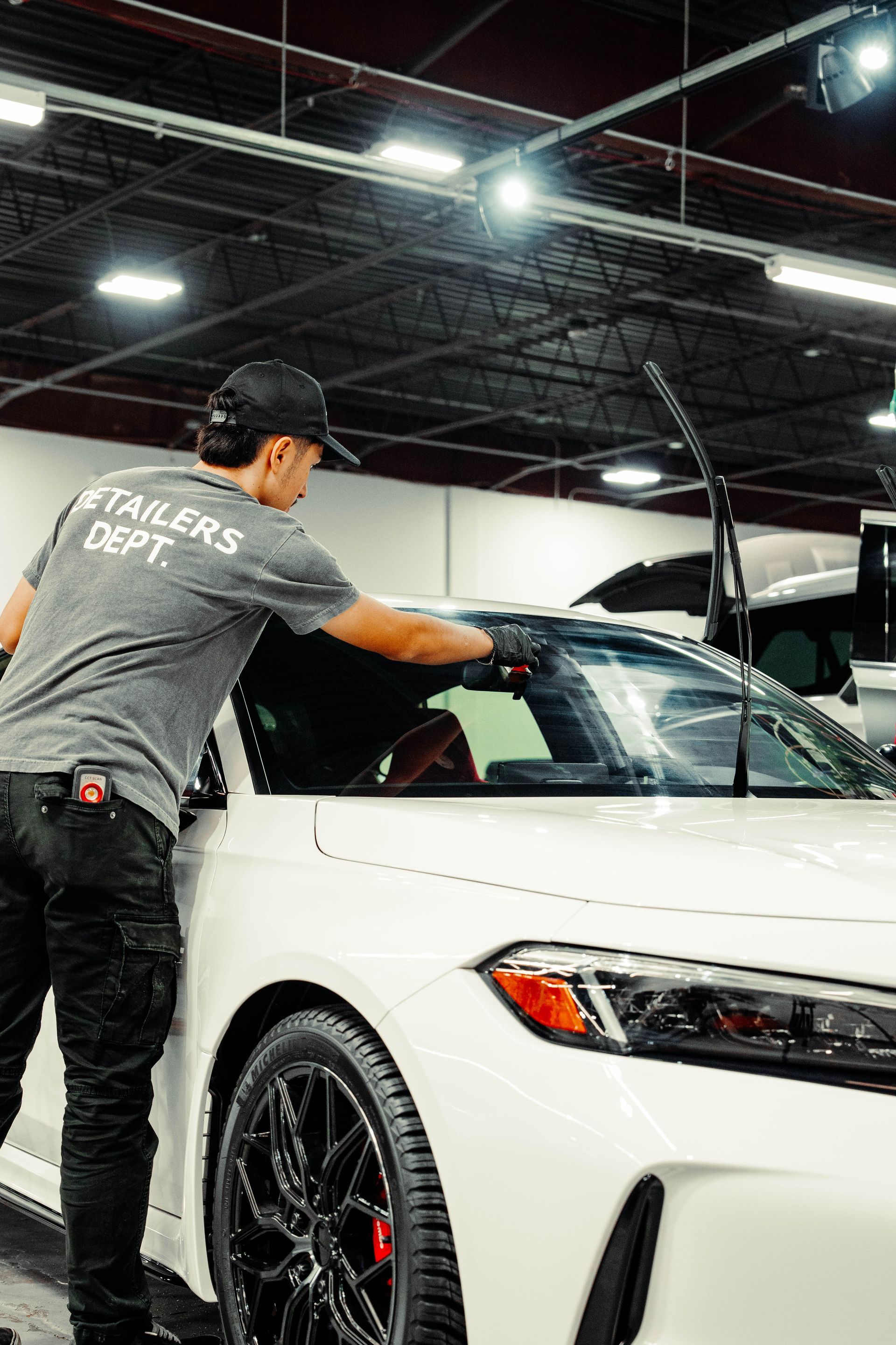 A man is cleaning the windshield of a white car in a garage.