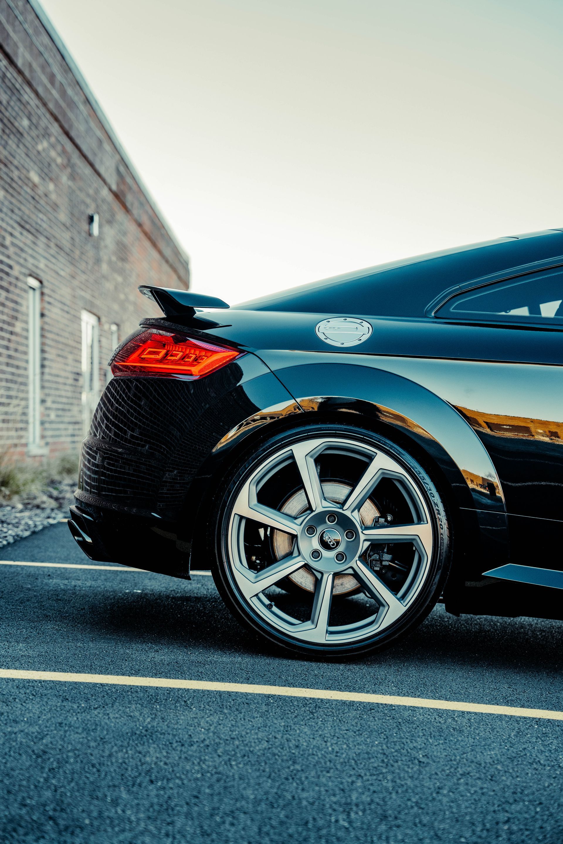 A black car is parked in a parking lot in front of a brick building.