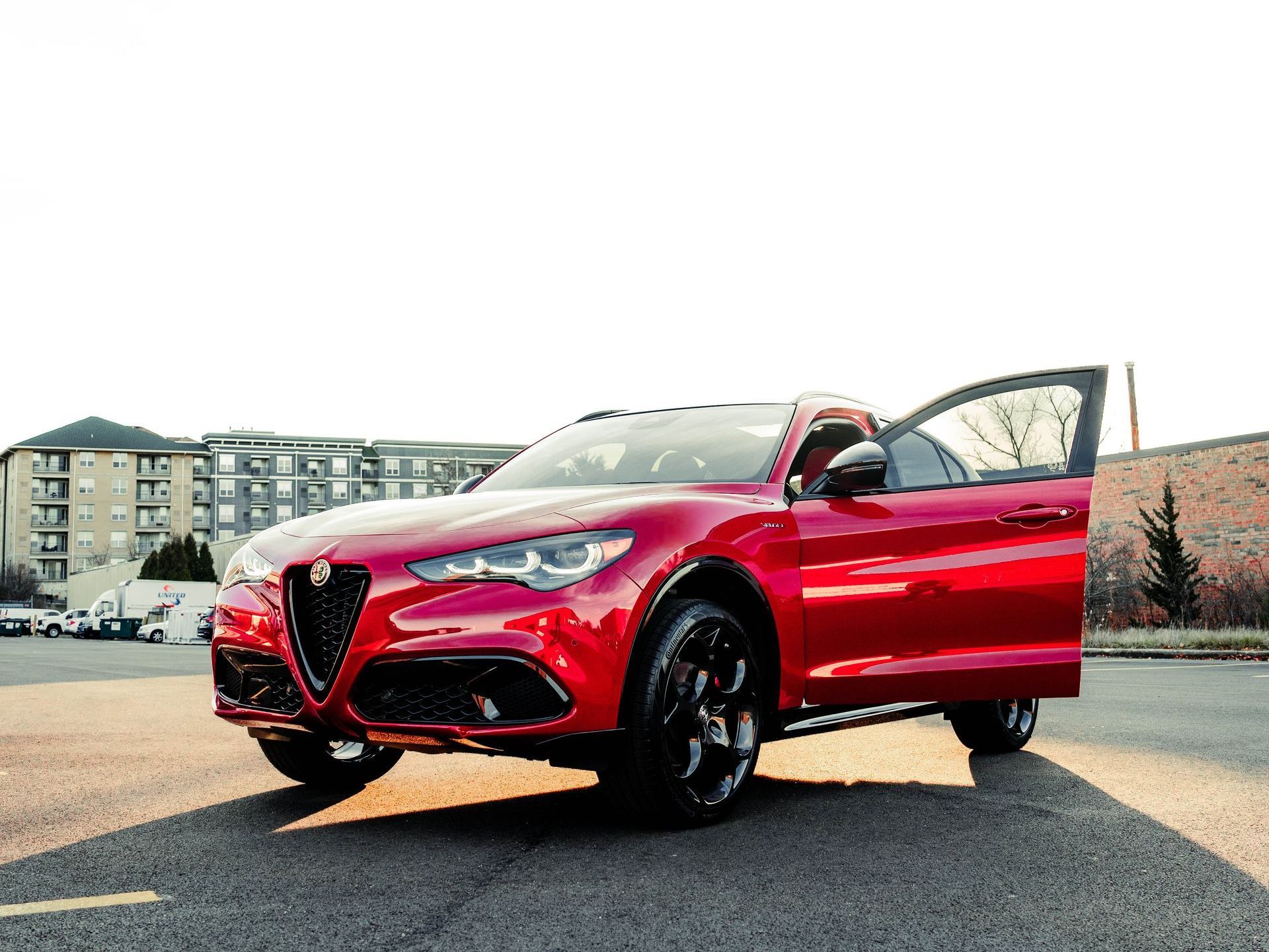 A red car  with black tint is parked on the side of the road with its doors open.