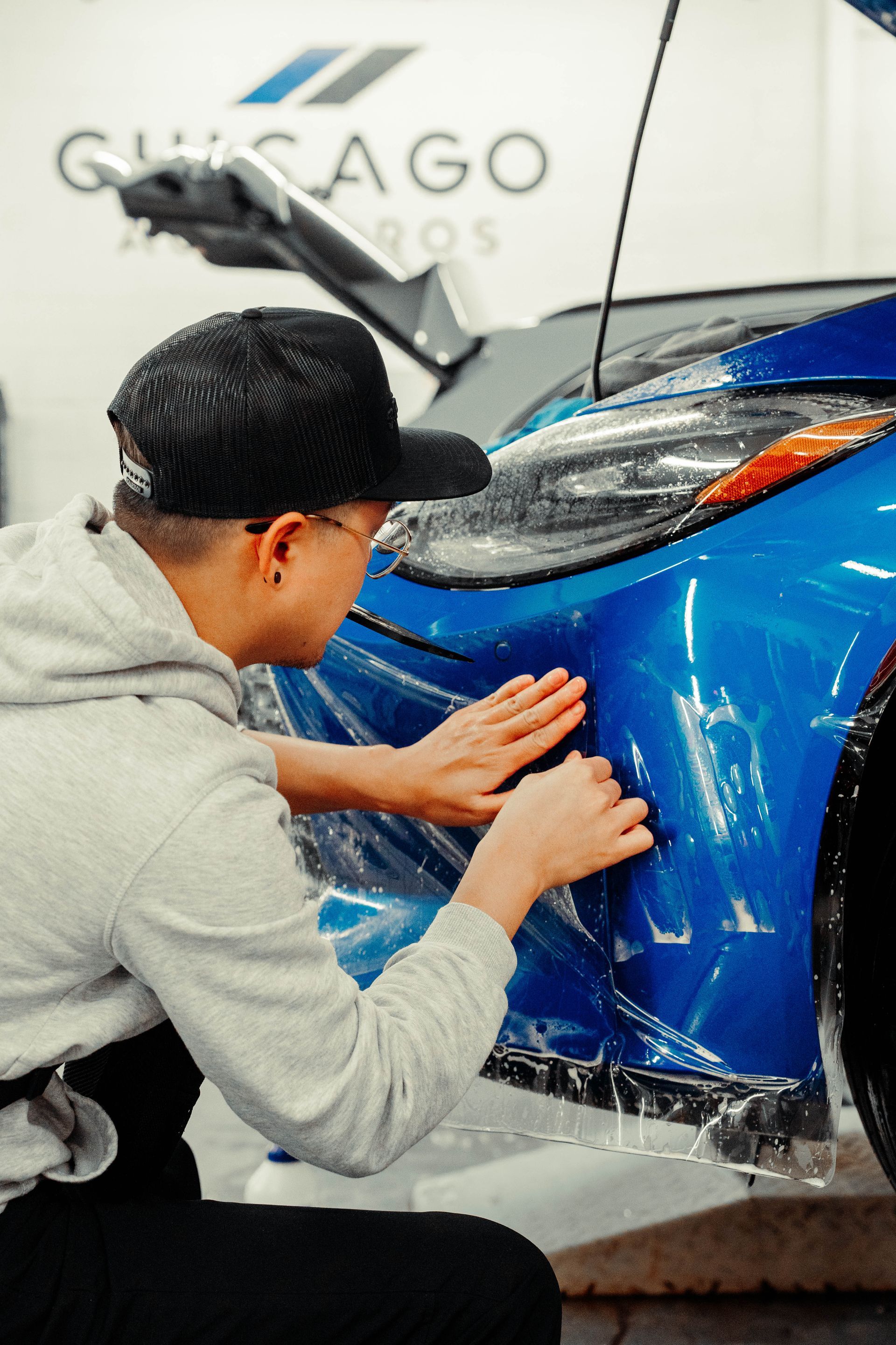 A man is wrapping a blue car with plastic wrap.