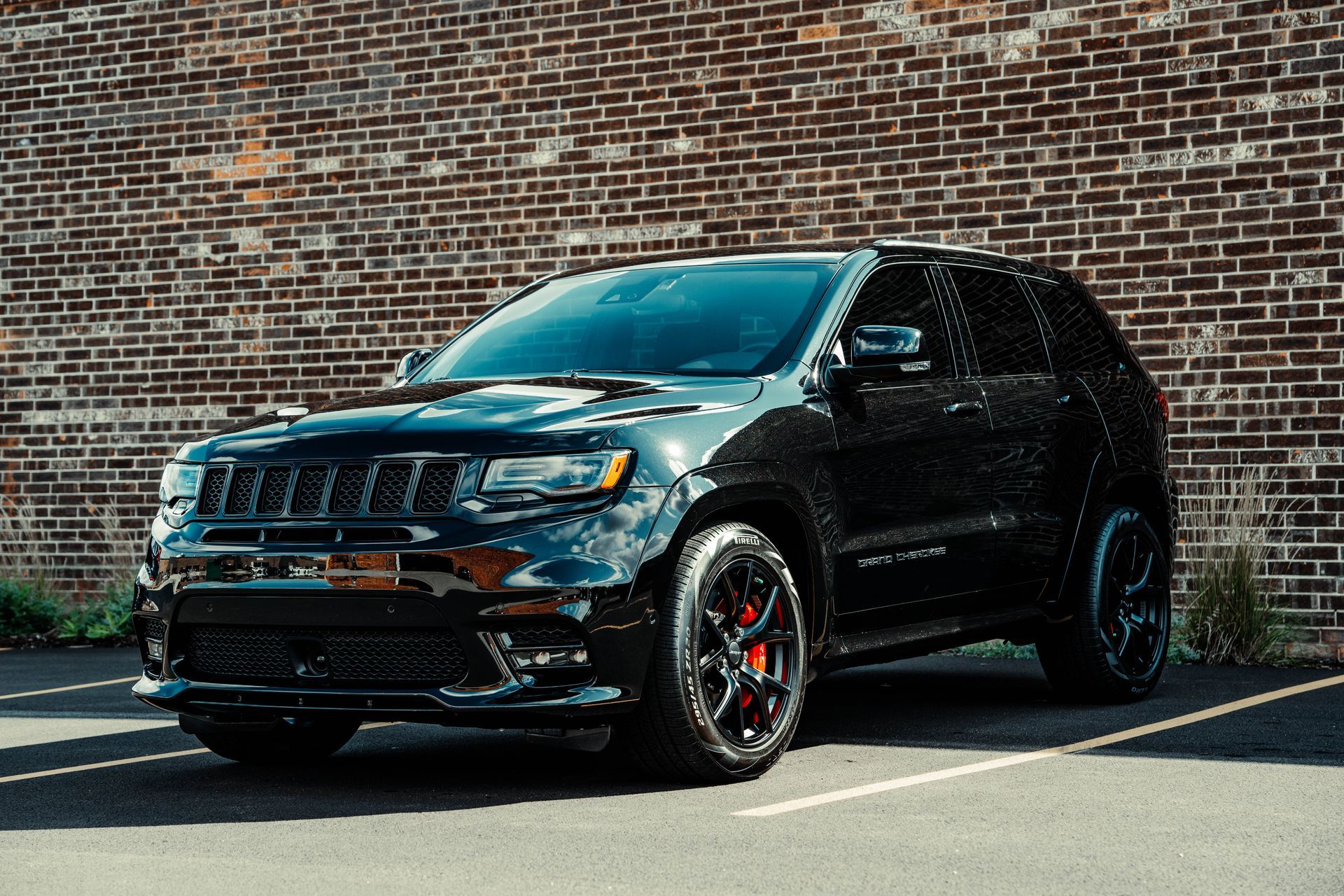 A black jeep grand cherokee is parked in front of a brick wall.