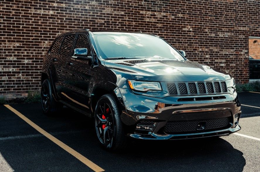 A black jeep grand cherokee is parked in a parking lot in front of a brick building.